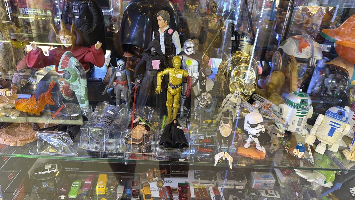 A glass display packed with vintage Star Wars figures, droids, ships, and collectible toys